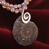 Ein peruanischer Ammonit an einem Ornament aus Rotgold in Verbindung mit einer Kette aus Süßwasserperlen